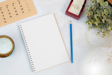 Top view flat lay wedding concept with notebook  mock up for checklist and pencil decorated with lace, beautiful pink rose bouquet flowers, calendar and coffee cup with copy space on white background