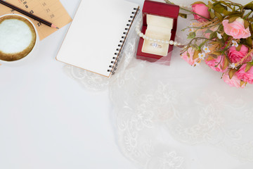 Top view flat lay wedding concept with notebook mock up for checklist and pencil decorated with lace, beautiful pink rose bouquet flowers, calendar and coffee cup with copy space on white background