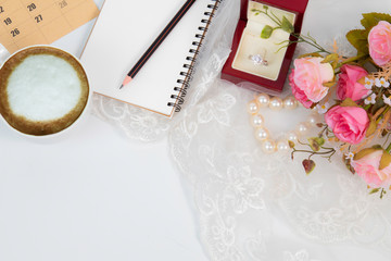 Naklejka premium Top view flat lay wedding concept with notebook mock up for checklist and pencil decorated with lace, beautiful pink rose bouquet flowers, calendar and coffee cup with copy space on white background