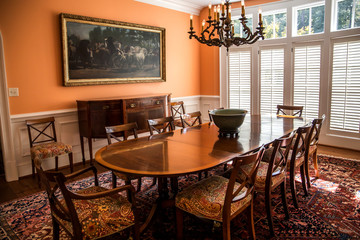 Orange peach colorful dining room with oriental rug and classic wood chairs and table with chandelier and artwork.