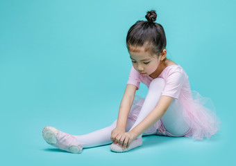 Beautiful smiling Asian little girl in a pink suit is dancing a ballet at school, empty space in...