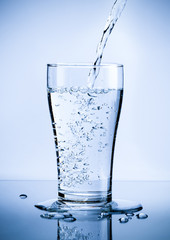 Pouring fresh pure water from bottle into a glass on the table with water drops, Healthcare and beauty hydration concept