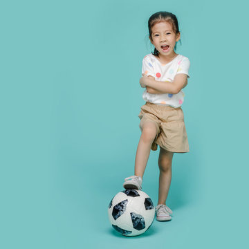 Excited Asian Little Girl Playing Football, Empty Space In Studio Shot Isolated On Colorful Blue Background