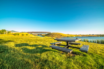 Picnic table with bench on the grassy shore of a beautiful lake on a sunny day