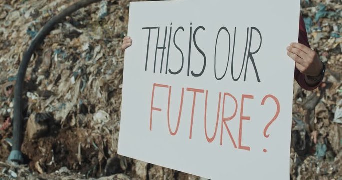 Close-up young man showing text of This Is Our Future poster striking against pollution on huge city landfill site. Environmentalism. Eco movement.