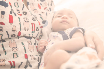 Soft focus of the Asian baby is sleeping in the arms of a mother with morning flare. A baby boy sleeping in the morning.