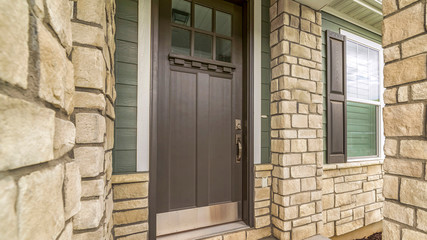 Panorama frame Home entrance with a glass paned brown wooden door and stone brick wall