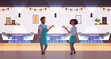 waiters couple carrying coffee and cake on tray african american woman man cafe workers barista in aprons holding cups of cappuccino with desserts modern cafeteria interior full length horizontal