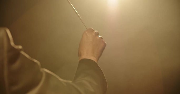 Close up shot of hand of unrecognizable orchesra conductor waving his stick and directing musicians during a rehearsal. Studio shot on black background 4k footage