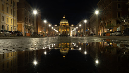 Vista nocturna del Vaticano desde La Via della Conciliacione reflejado en un charco del suelo