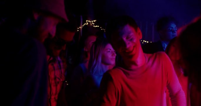 At colorful light young multi-ethnic people dance party in different clothes drinking alcohol having fun on weekend laughing sharing socializing celebration close up slow motion