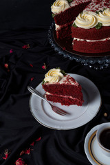 Pedazo de Torta Red Velvet en un fondo dramático con mantel rojo y tetera blanca. Crema y dulce  sobre el postre. 