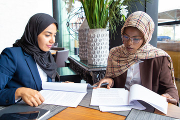 Confident female professionals checking documents. Young Muslim business women sitting in cafe and...