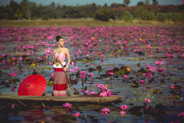Asia women on the boat in the lotus pond. She wears Thai traditional dresses.