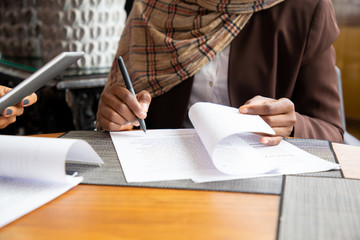 Muslim businesswoman signing contract. Business women wearing hijabs, sitting in cafe and writing...