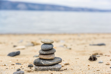 Fototapeta na wymiar Stones balances on the beach of blue sea with mountain