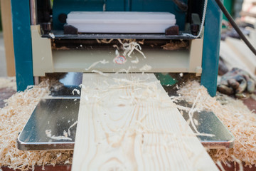 planing boards on a thicknesser. wood shavings. machine for planing wood. carpentry work. joiner's machine.