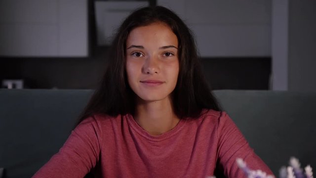 smiling dark haired girl in purple sweatshirt tells interesting things and shows different gestures in videochat closeup