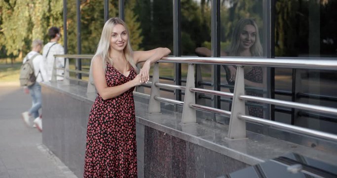 Young beautiful long-haired blonde in a long dress on the glass building background.
