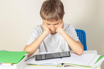 Naklejka premium Kid sitting at table with books notebooks and using tablet computer