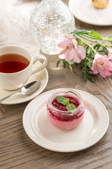 Strawberry jam in a jar and cup of black tea on wooden table
