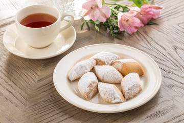 Shortbread cookies with icing sugar on the plate and cup of black tea on wooden table