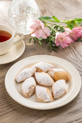 Shortbread cookies with icing sugar on the plate and cup of black tea on wooden table