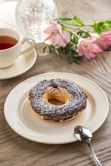 custard cake with chocolate icing and cup of black tea and flowers on wooden table