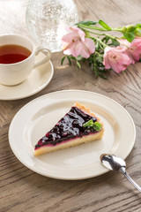 piece of blueberry cheesecake with cup of black tea and flowers on wooden table