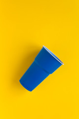 Dark blue plastic single use cup on yellow background. Concept of recycling plastic and ecology. Top view.