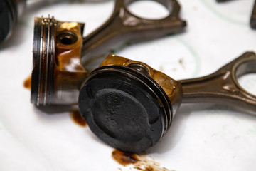 Two metal car pistons in poor condition with soot oil removed from used engine in a deposit of oil lying on workbench in a vehicle repair shop for washing and restoration. High engine oil consumption.