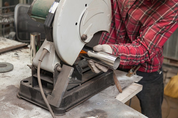 A male worker cuts a stainless steel pipe on a special machine for vertical sawing of metal parts for industrial use. Making exhaust for a car.
