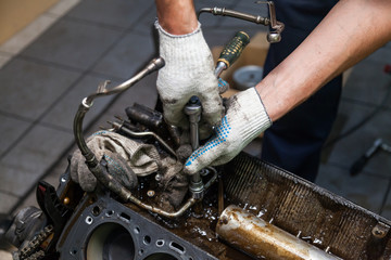 A car repair and maintenance specialist unscrews a bolt with a wrench on an 8-cylinder engine in a workshop. Auto service industry.