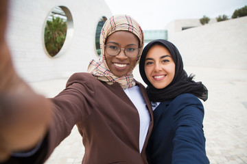 Cheerful female corporate friends taking selfie outside. Self picture of Muslim business women in...