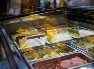 Slices of cake and various flavors of ice cream displayed in cafe fridge