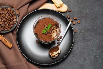 Portion of Classic tiramisu dessert in a glass cup on dark concrete background