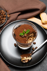 Portion of Classic tiramisu dessert in a glass cup on dark concrete background
