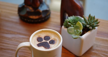 Cat paw pattern latte art coffee in white mug on wood table with succulent plant decoration in cafe