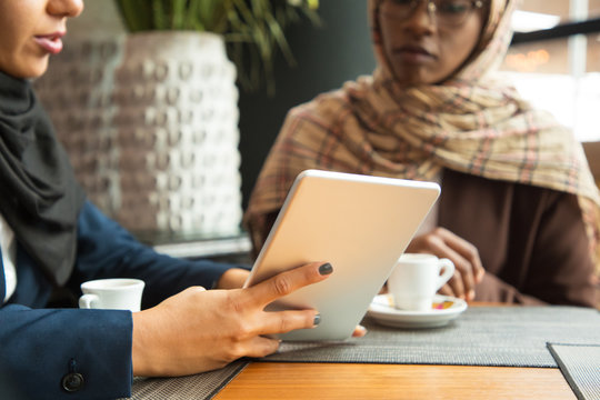 Female colleagues watching content on tablet in coffee shop. Muslim business women in hijabs sitting in cafe, using tablet together, looking at screen. Interaction concept