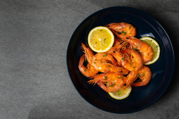 Boiled shrimp with lemon and parsley in blue plate on concrete table.