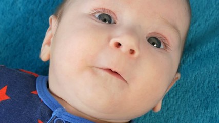 Portrait of beautiful funny little newborn baby of two months lying on blue bedspread surrounded by baby rattles