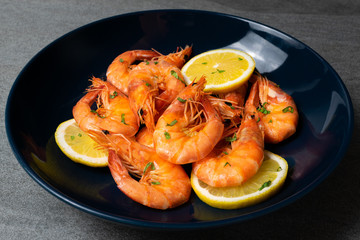 Boiled shrimp with lemon and parsley in blue plate on concrete table.