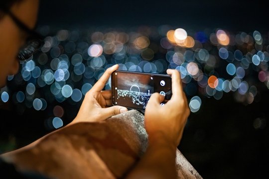 Guy taking picture of the cite with smartphone at night