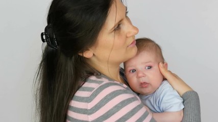 Young beautiful mother with long dark hair is holding a newborn infant baby of two months on a white background in studio