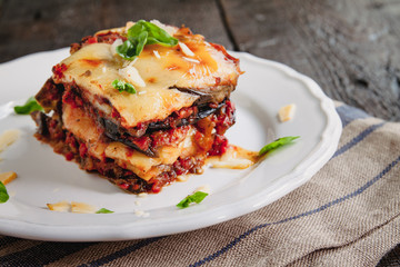 tradicional Parmigiana di melanzane: baked eggplant - italy, sicily cousine.Baked eggplant with cheese, tomatoes and spices on a white plate. A dish of eggplant is on a wooden table - 287892246