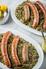 Norddeutscher Grünkohl und regionale Kohlwurst Variation aus Bremer, Oldenburger und Ammerländer Pinkel auf Platten mit Kartoffeln und Senf auf Marmor Tisch