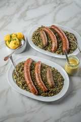 Norddeutscher Grünkohl und regionale Kohlwurst Variation aus Bremer, Oldenburger und Ammerländer Pinkel auf Platten mit Kartoffeln und Senf auf Marmor Tisch
