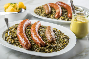Norddeutscher Grünkohl und regionale Kohlwurst Variation aus Bremer, Oldenburger und Ammerländer Pinkel auf Platten mit Kartoffeln und Senf auf Marmor Tisch