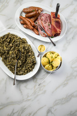 Oldenburger Grünkohl, Kassler Nacken, Kohlwurst und Pinkel auf Platten mit Kartoffeln und Senf auf Marmor Tisch