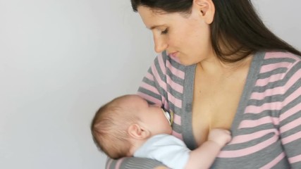 Young beautiful mother with long dark hair is holding a newborn infant baby of two months on a white background in studio